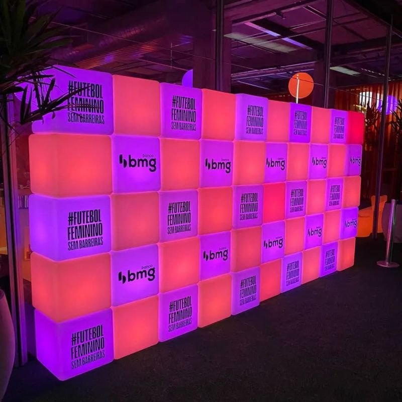Parede de cubos LED em rosa e roxo com a marca do banco bmg e a frase Futebol Feminino Sem Barreiras