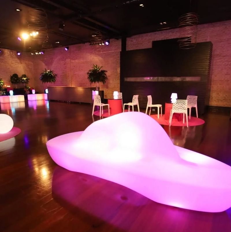 Banco LED de formas orgânicas, com 2,60 m, aceso em rosa num salão de festas com piso de madeira
