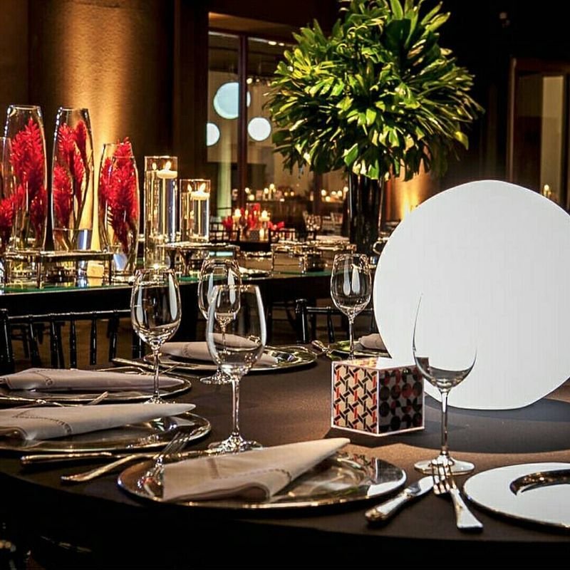 Mesa posta com taças, velas e flores vermelhas, com uma esfera LED branca iluminando o centro