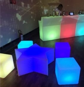 Puff LED em forma de estrela aceso em azul-violeta entre cubos LED coloridos, diante de um balcão iluminado