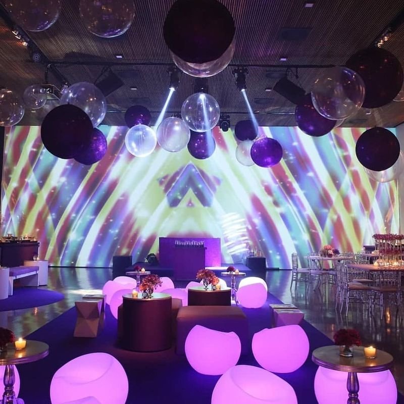 Pista de festa com projeções e puffs LED redondos acesos em rosa e lilás