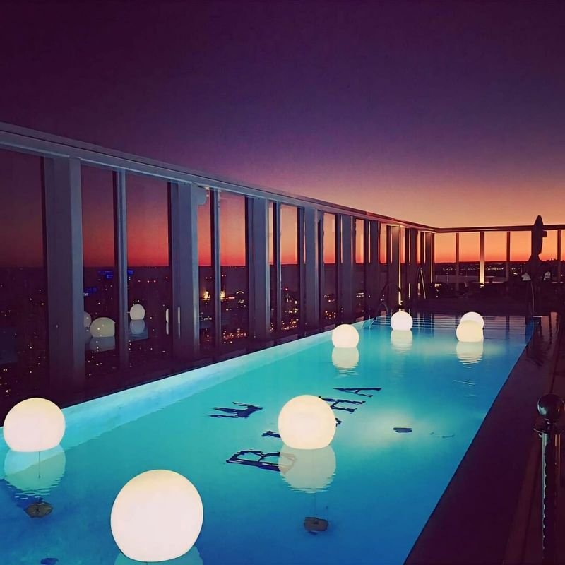 Piscina de cobertura ao entardecer com esferas LED acesas em branco quente boiando, refletidas na água