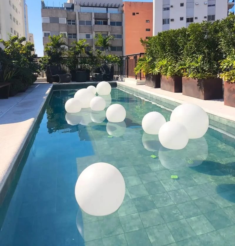 Esferas LED brancas boiando numa piscina de azulejos durante o dia, com a parte de baixo visível sob a água